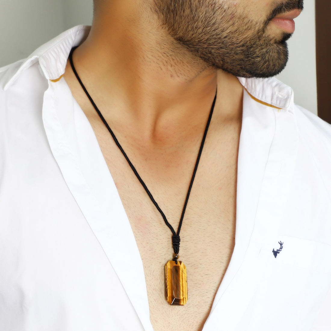 A close-up view of the pendant necklace showcasing the smooth baguette-shaped tiger's eye gemstone wrapped with an adjustable rope necklace, displaying its captivating golden hues.