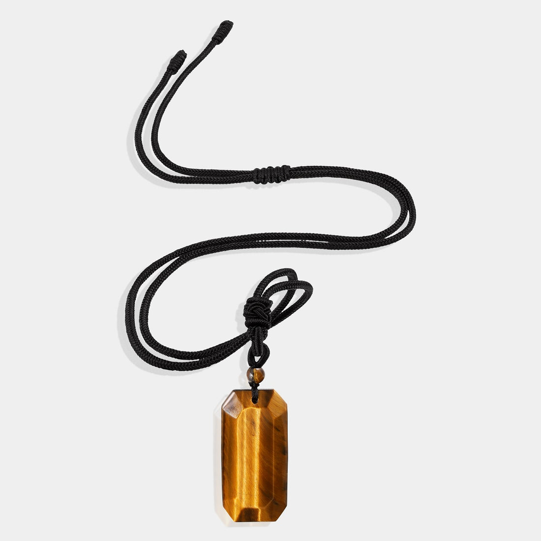 A close-up view of the pendant necklace showcasing the smooth baguette-shaped tiger's eye gemstone wrapped with an adjustable rope necklace, displaying its captivating golden hues.