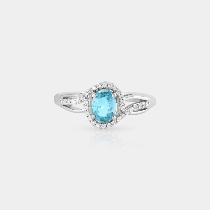 the 5x7mm oval Blue Zircon, showcasing its deep blue hue and precise prong setting Detailed shot featuring the halo design with 34 prong-set 1mm White Zircon accents, emphasizing the sparkling brilliance